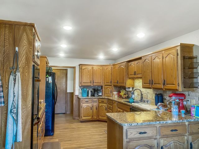 A kitchen with wooden cabinets , granite counter tops , a refrigerator and a sink.