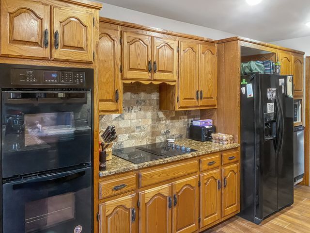 A kitchen with wooden cabinets , stainless steel appliances , a black refrigerator and a black oven.