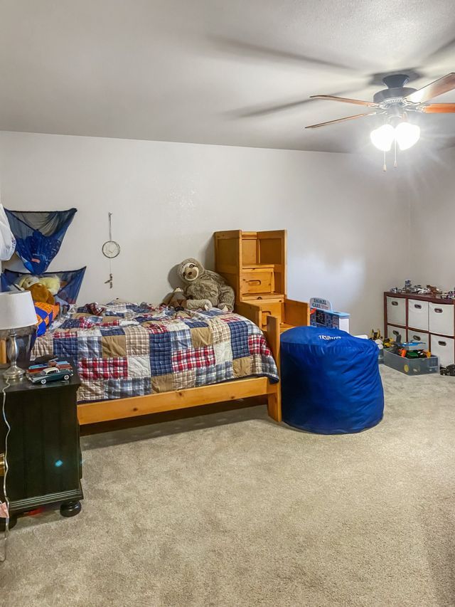 A bedroom with a bed , a ceiling fan , a blue bean bag chair , and a shelf.