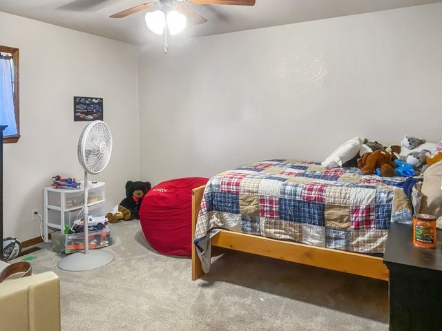 A bedroom with a bed , a fan , and a red bean bag chair.