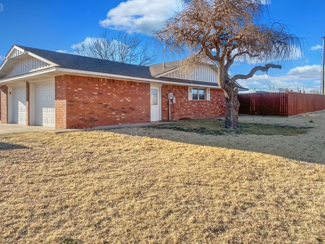 A brick house with a garage and a tree in front of it.