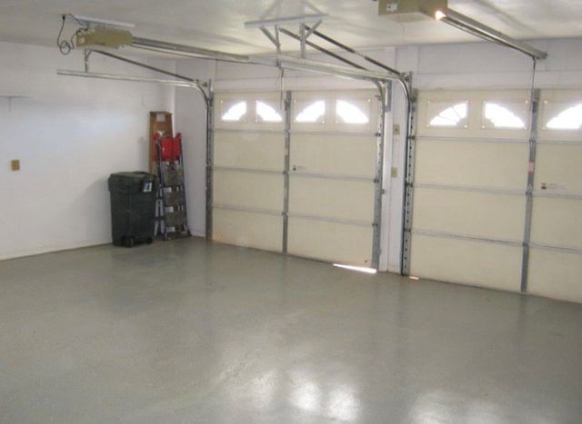 An empty garage with two garage doors open and a trash can in the corner.
