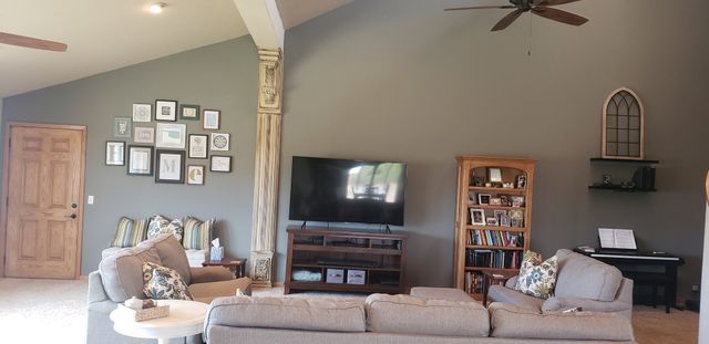 A living room with a couch , chairs , a television and a ceiling fan.