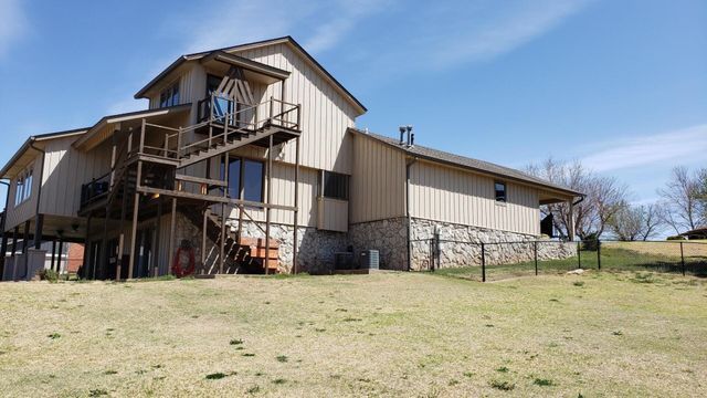 A large house with stairs leading up to the second floor is sitting on top of a grassy hill.