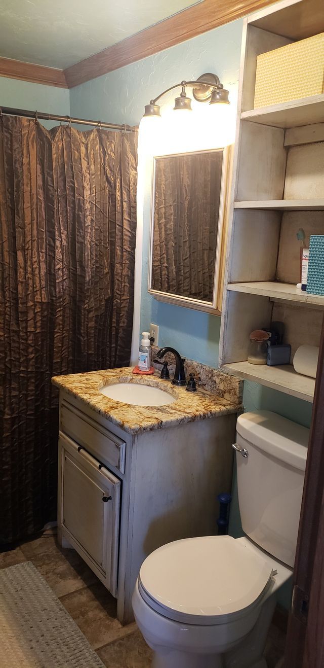A bathroom with a toilet , sink , mirror and shelves.