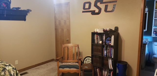 A room with a chair , bookshelf , and a sign on the wall.