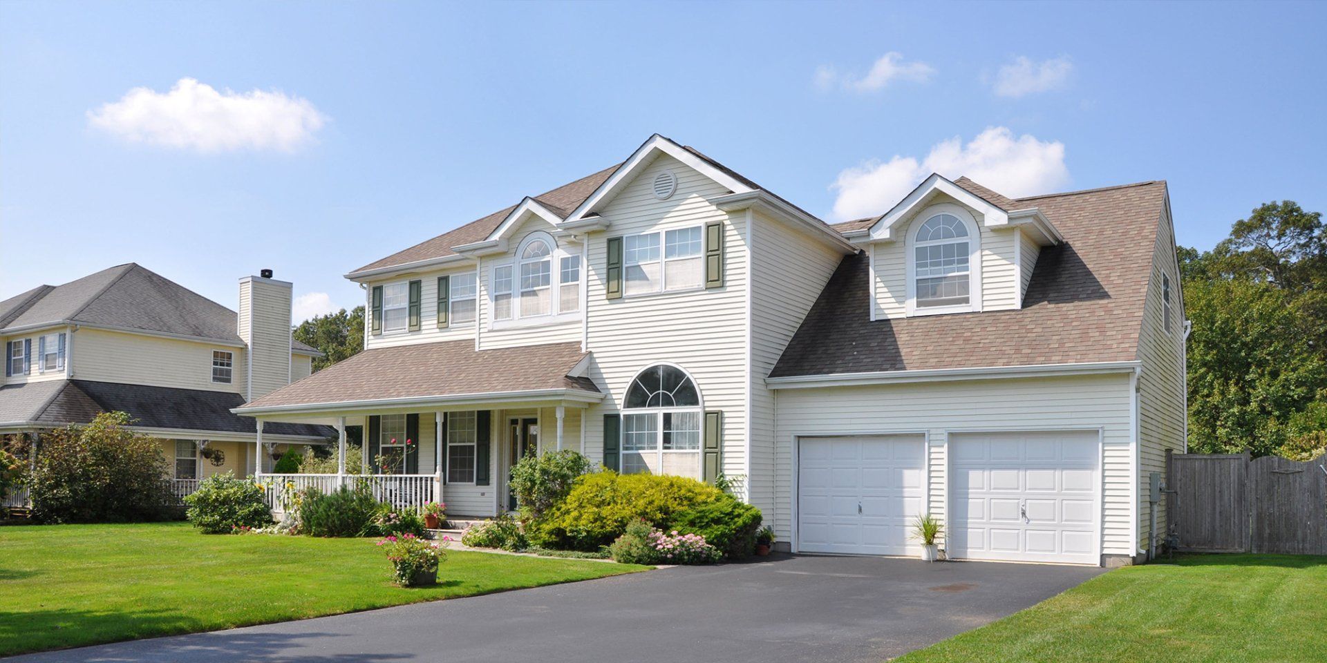 A large white house with a brown roof and two garages