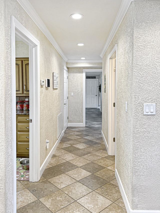 A long hallway with a checkered tile floor leading to a kitchen.