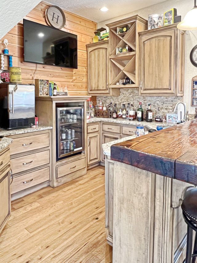 A kitchen with wooden cabinets , granite counter tops , a refrigerator and a flat screen tv.