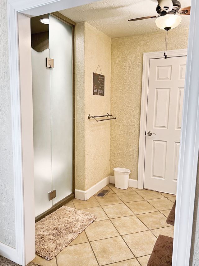 A bathroom with a walk in shower and a ceiling fan.