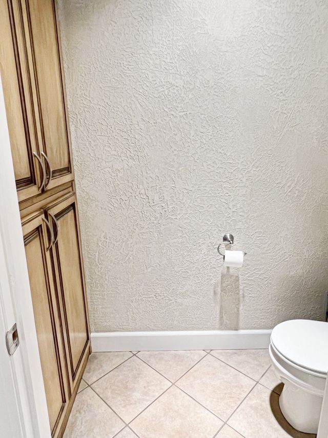 A bathroom with a toilet , cabinets , and tile floor.