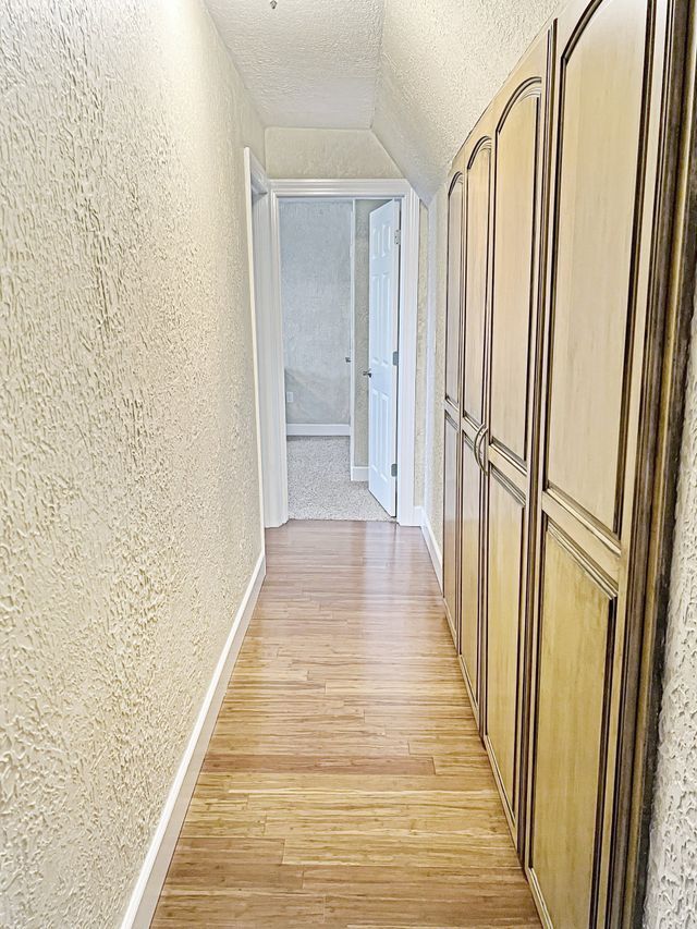 A long hallway with wooden floors and white walls leading to a bathroom.