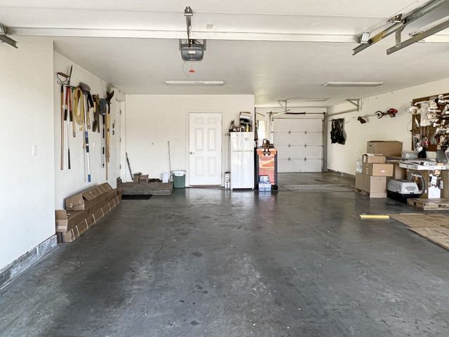 An empty garage with a refrigerator , boxes , and tools.