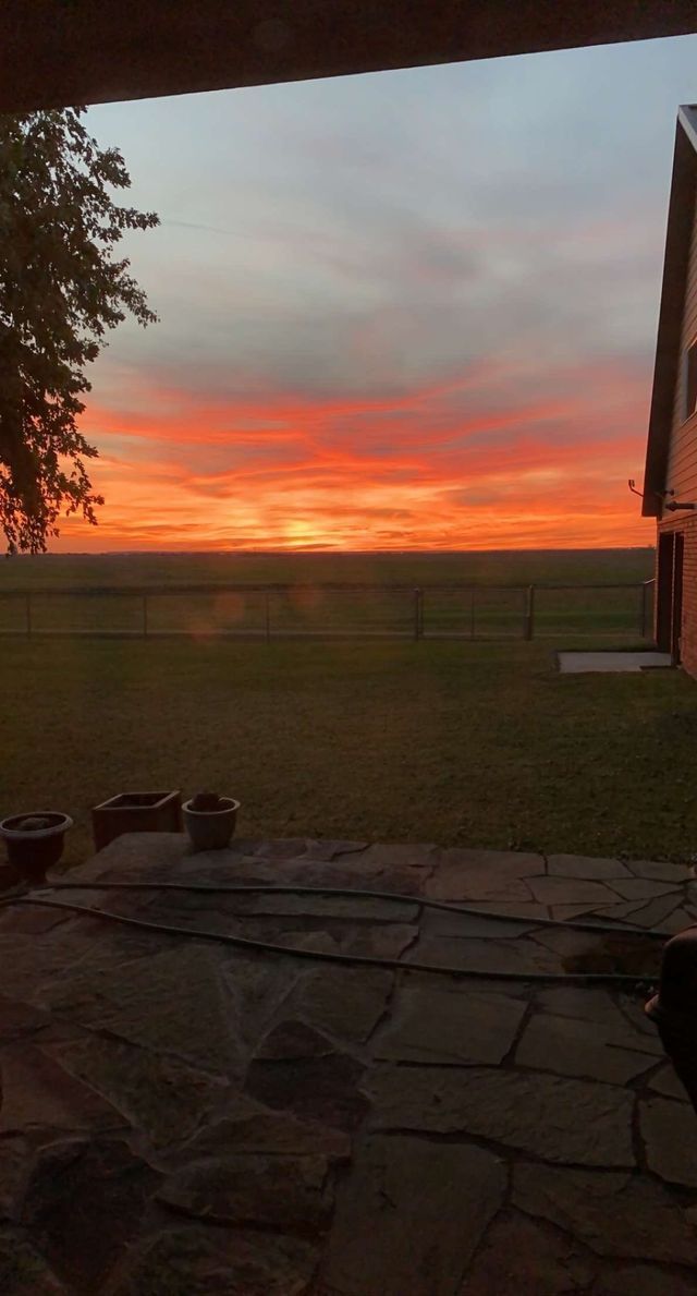 A sunset over a field with a house in the background