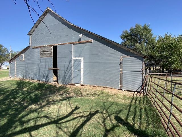 A gray barn is sitting in the middle of a grassy field