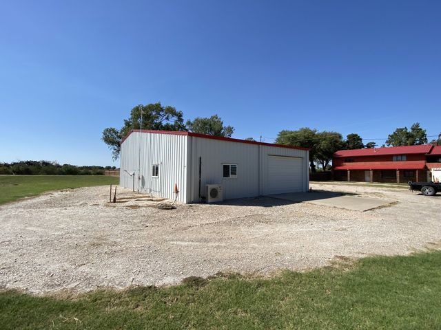 A white building with a red roof is in the middle of a dirt field.