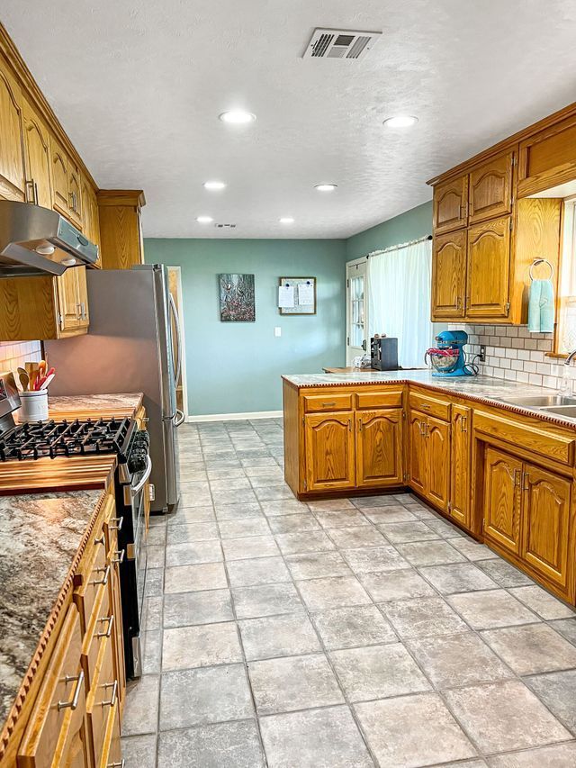 A kitchen with wooden cabinets , granite counter tops , a stove and a refrigerator.