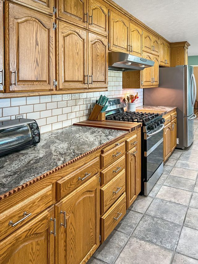 A kitchen with wooden cabinets , granite counter tops , a stove and a refrigerator.