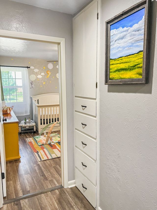 A hallway leading to a bedroom with a crib and a painting on the wall.