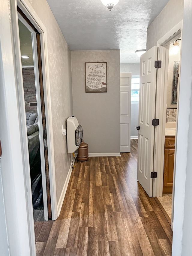 A hallway with hardwood floors leading to a bathroom and a living room.