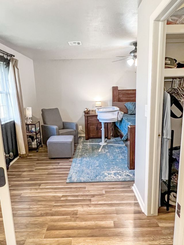 A living room with hardwood floors , a crib , a chair , and a closet.