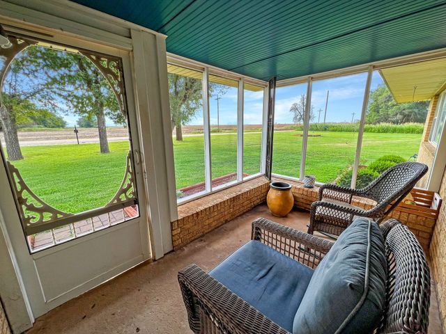 A screened in porch with a chair and ottoman and a view of a field.