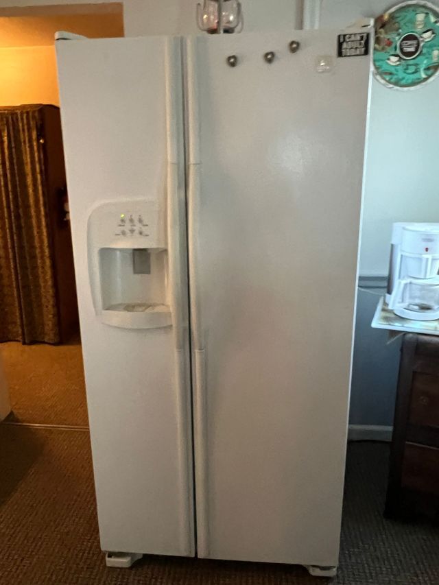 A white refrigerator with a water dispenser is sitting in a kitchen.