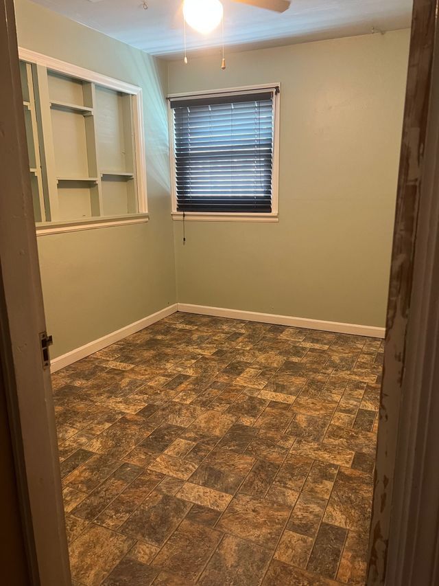 An empty room with a window and a ceiling fan.