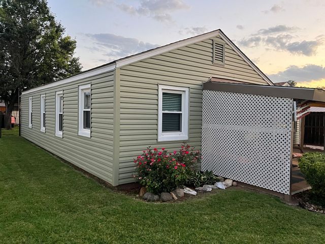 A mobile home with a green siding and white windows is sitting on top of a lush green lawn.