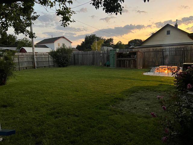 A backyard with a fence and a fire pit at sunset