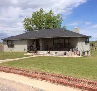 A white house with a black roof and a brick fence in front of it.