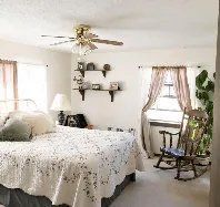 A bedroom with a large bed , rocking chair , and ceiling fan.