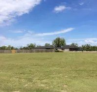 A large grassy field with a house in the background on a sunny day.