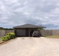 A car is parked under a canopy in front of a house.