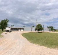 A truck is parked in front of a large building on a dirt road.