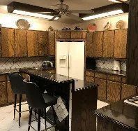 A kitchen with wooden cabinets , granite counter tops , a refrigerator and a ceiling fan.