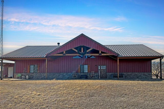 A large red barn with a metal roof is sitting in the middle of a field.
