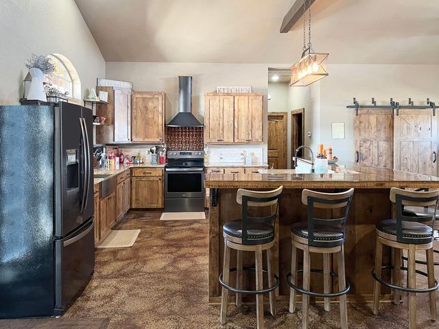 A kitchen with a large island , stools , a refrigerator and a stove.