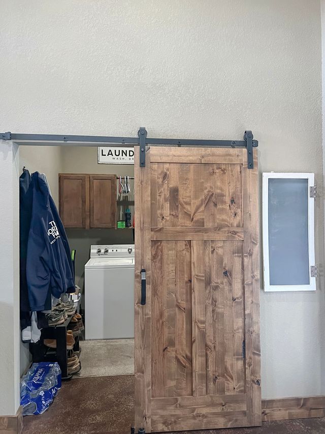 A sliding barn door is open to a laundry room with a washer and dryer.