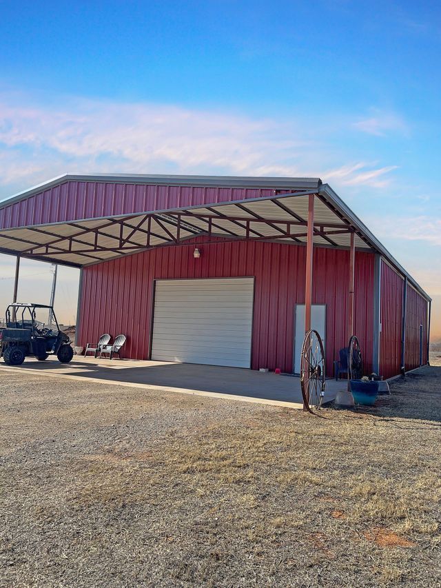 A red barn with a covered area and a jeep parked in front of it.