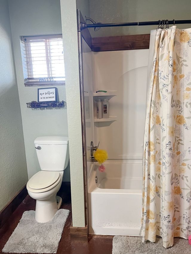 A bathroom with a toilet , bathtub , shower and window.