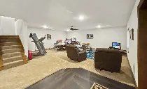 A living room with a treadmill and stairs in a basement.