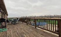 A large wooden deck with a fence and chairs on it.