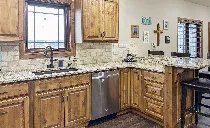 A kitchen with granite counter tops , wooden cabinets , stainless steel appliances and a window.
