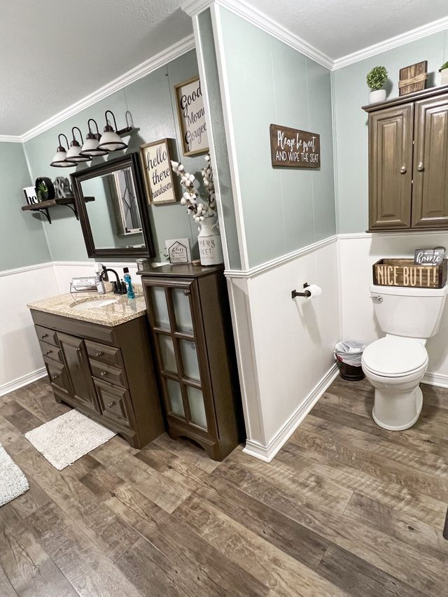 A bathroom with a toilet , sink , mirror and cabinets.
