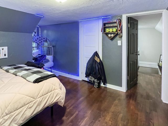 A bedroom with a bed , wooden floor , and a blue light on the wall.