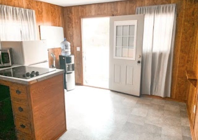 A kitchen with a stove , sink , microwave and door.