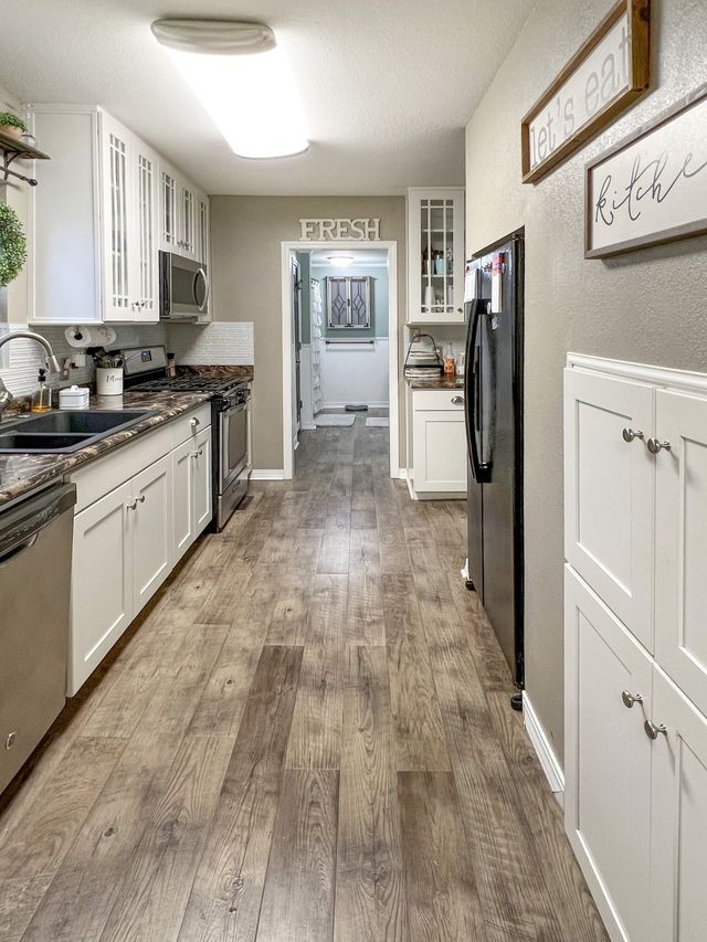 A kitchen with hardwood floors , white cabinets and stainless steel appliances.
