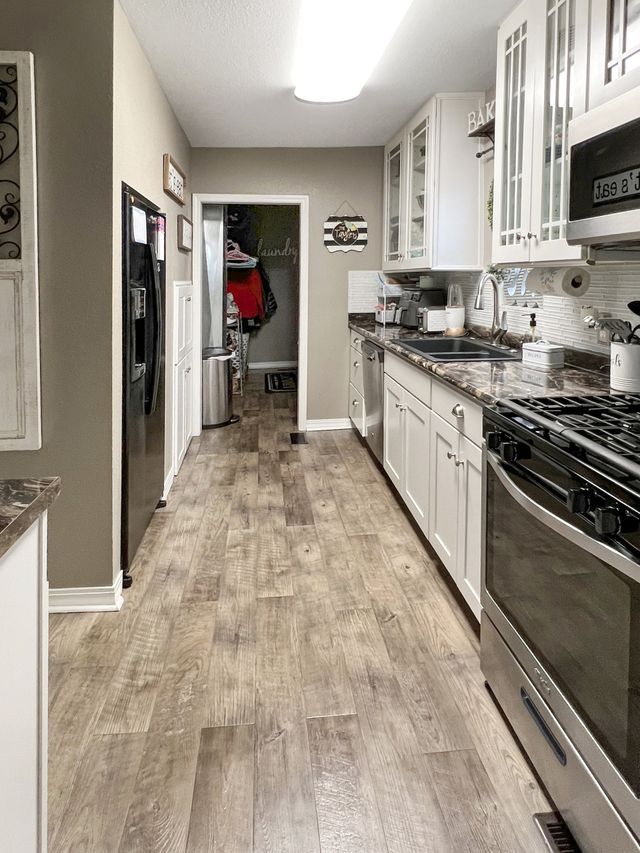 A kitchen with hardwood floors , stainless steel appliances , and white cabinets.