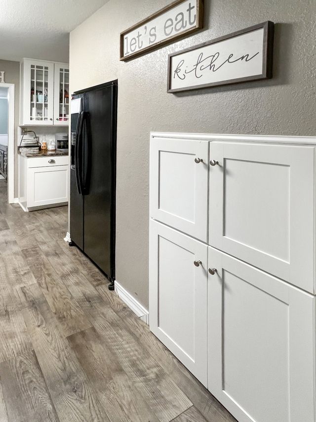 A kitchen with a black refrigerator and white cabinets.